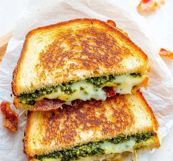 Pesto grilled cheese sandwich on a plate, garnished with fresh basil.